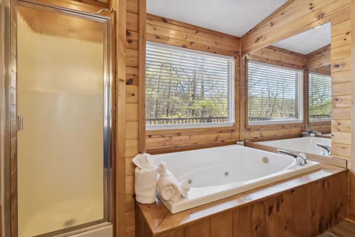 A serene ensuite bathroom with a sparkling jacuzzi tub and modern shower, surrounded by natural wood paneling and bathed in natural light from generous windows. The spa-like ambiance invites relaxation and self-care.