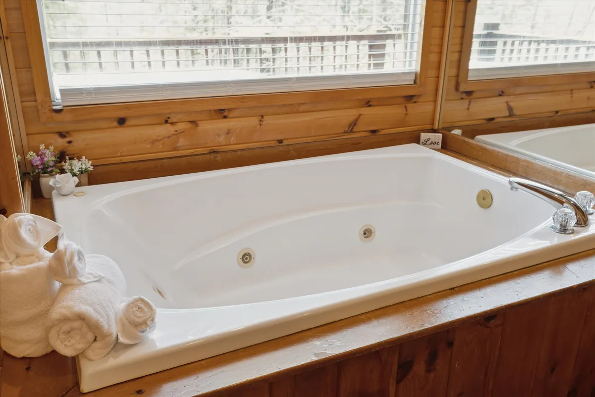 A tranquil whirlpool bathtub scene, featuring fluffy towels and a delicate flower arrangement by a window. The setting suggests unwinding with a soothing soak, perhaps accompanied by a glass of wine and a scenic view.
